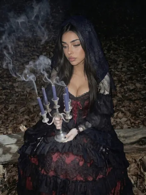 Eliza in a hooded gown holding a smoking candelabra